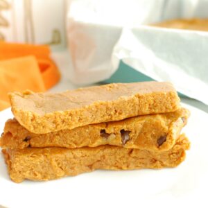 Three pumpkin protein bars stacked on top of each other on a white plate.