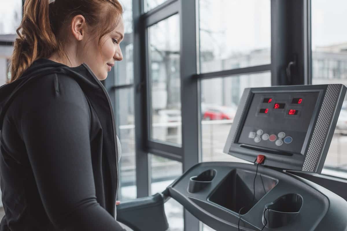 A woman in a sweatshirt stepping onto the treadmill.