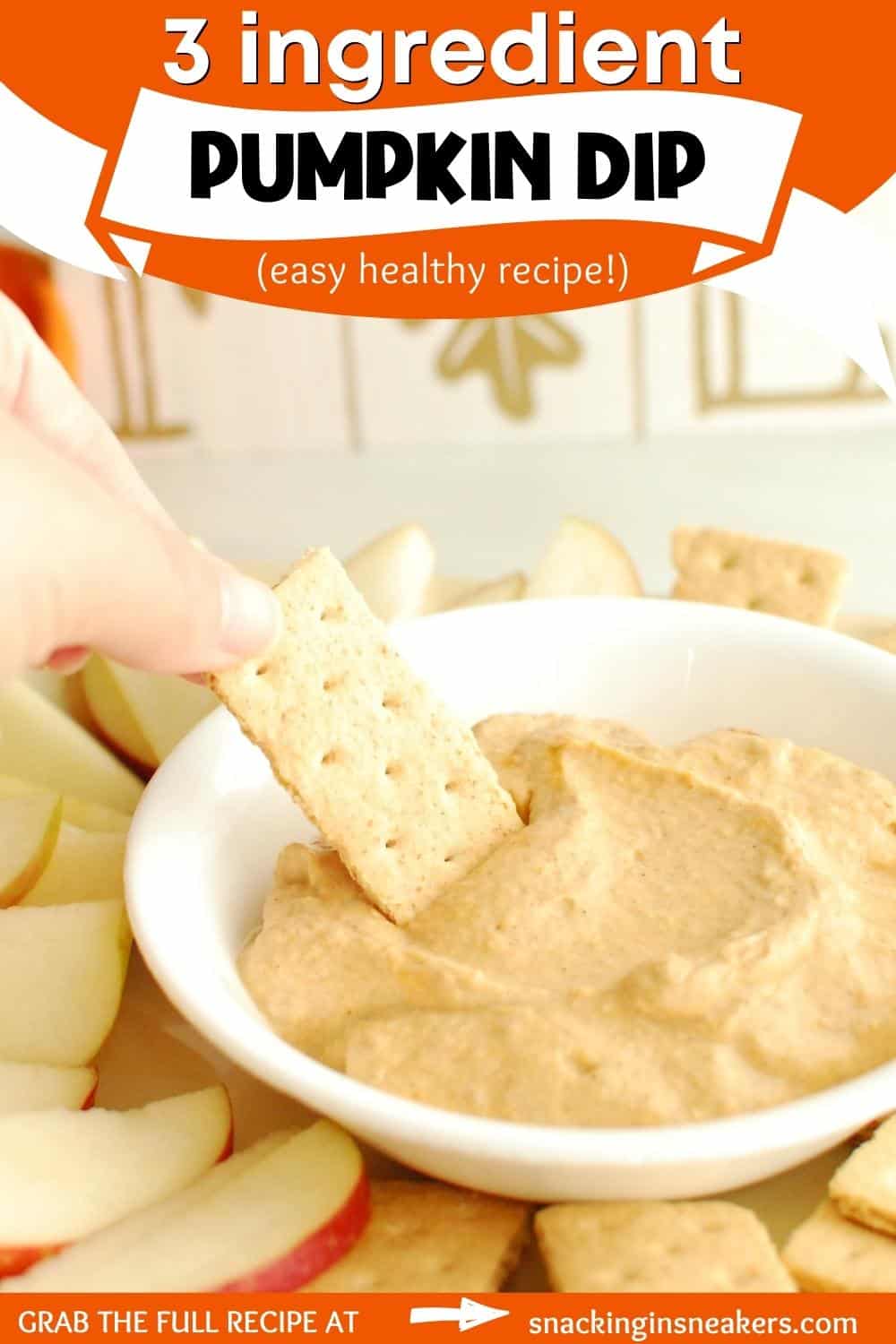 A woman's hand dipping a graham cracker into a bowl of pumpkin greek yogurt dip.