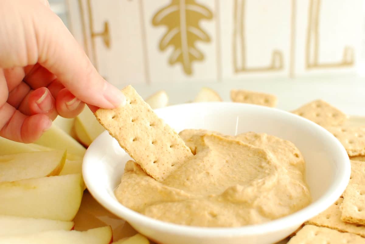 A woman dipping a graham cracker into healthy pumpkin dip.