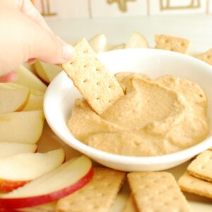 A hand dipping a graham cracker into a bowl of pumpkin greek yogurt dip.