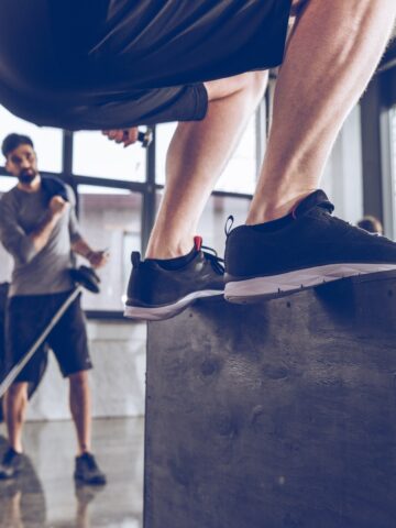 A person jumping onto a box at a gym.