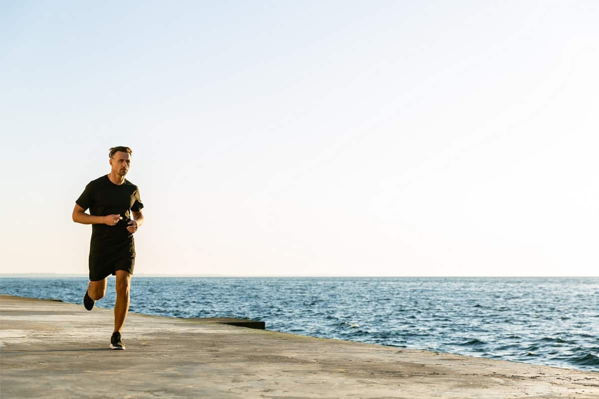 A man running on a paved path by the waterfront.