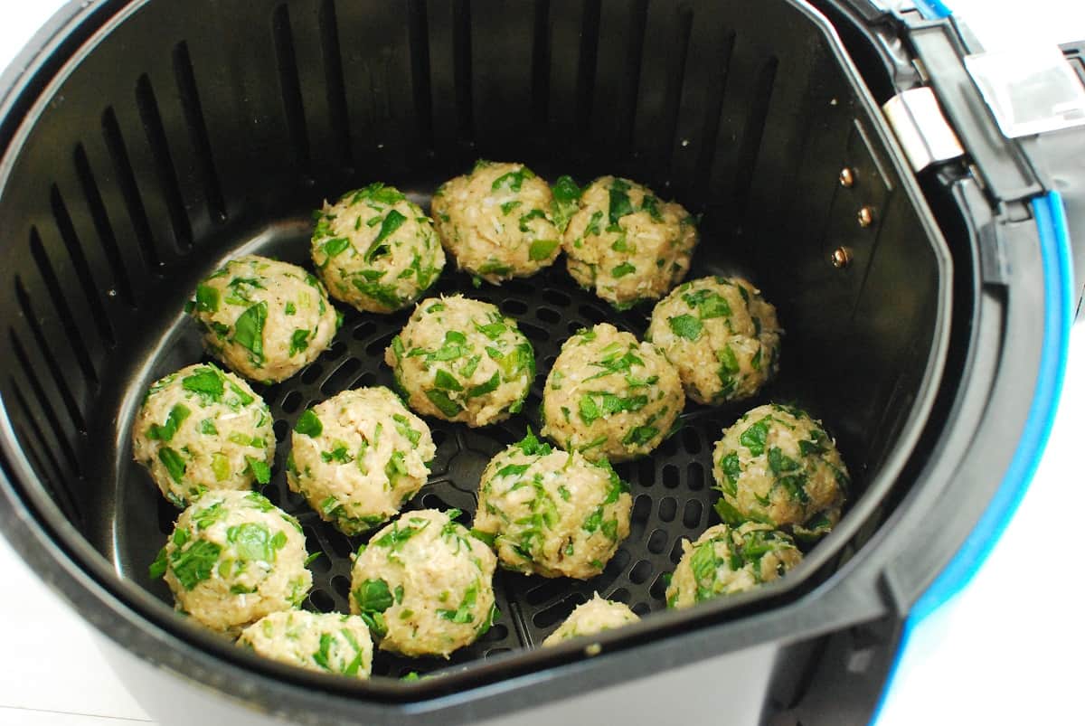 Uncooked meatballs in an air fryer basket.