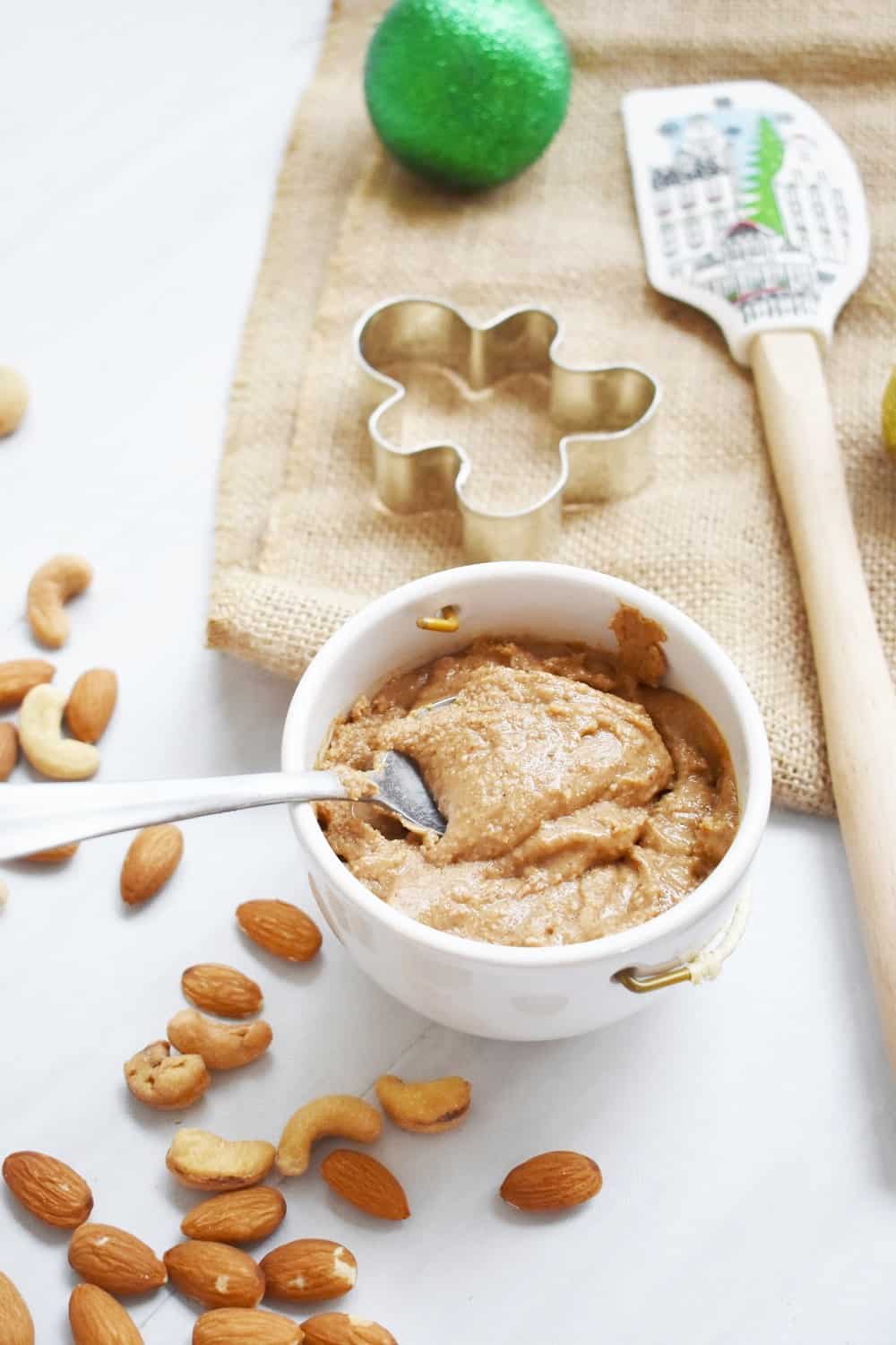 A cup full of homemade gingerbread almond cashew butter next to nuts.