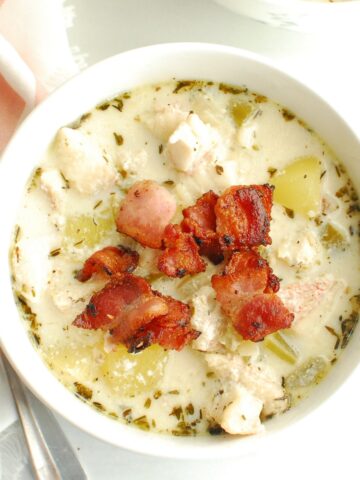 A bowl of redfish chowder next to a napkin and spoon.