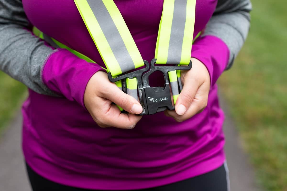 A woman clipping on a reflective running vest.