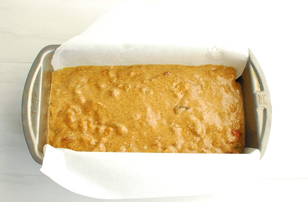 Unbaked fruitcake batter in a loaf pan lined with parchment paper.