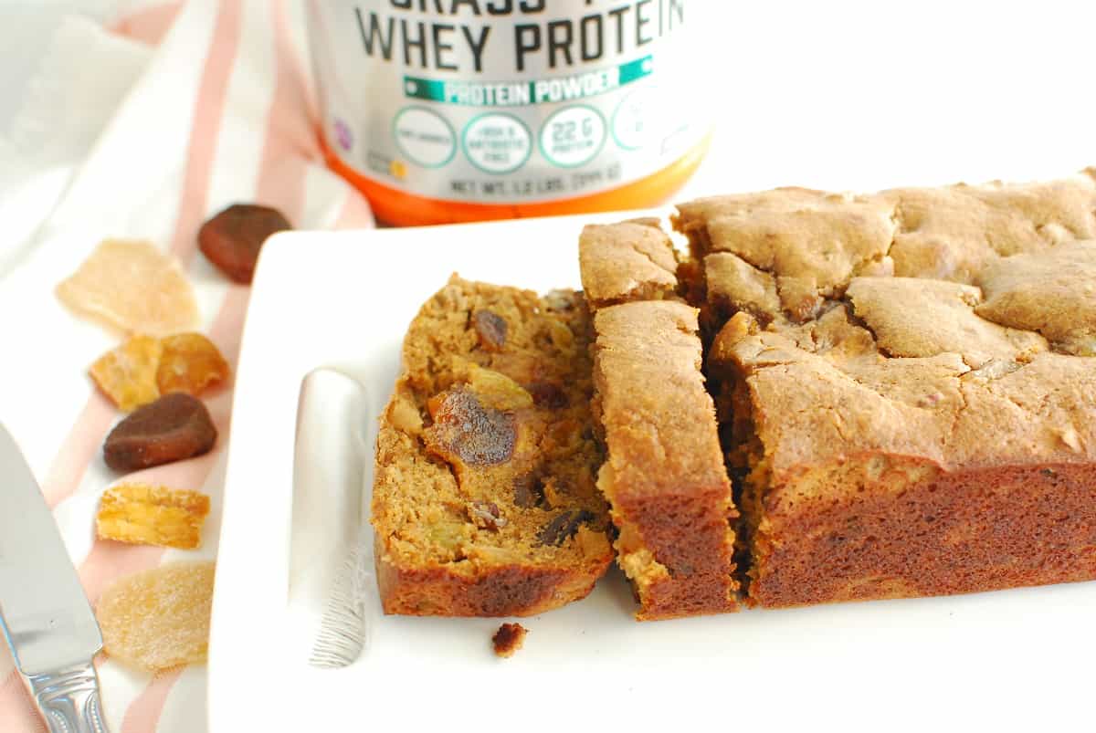 A slice of fruitcake on a white plate with protein powder in the background.