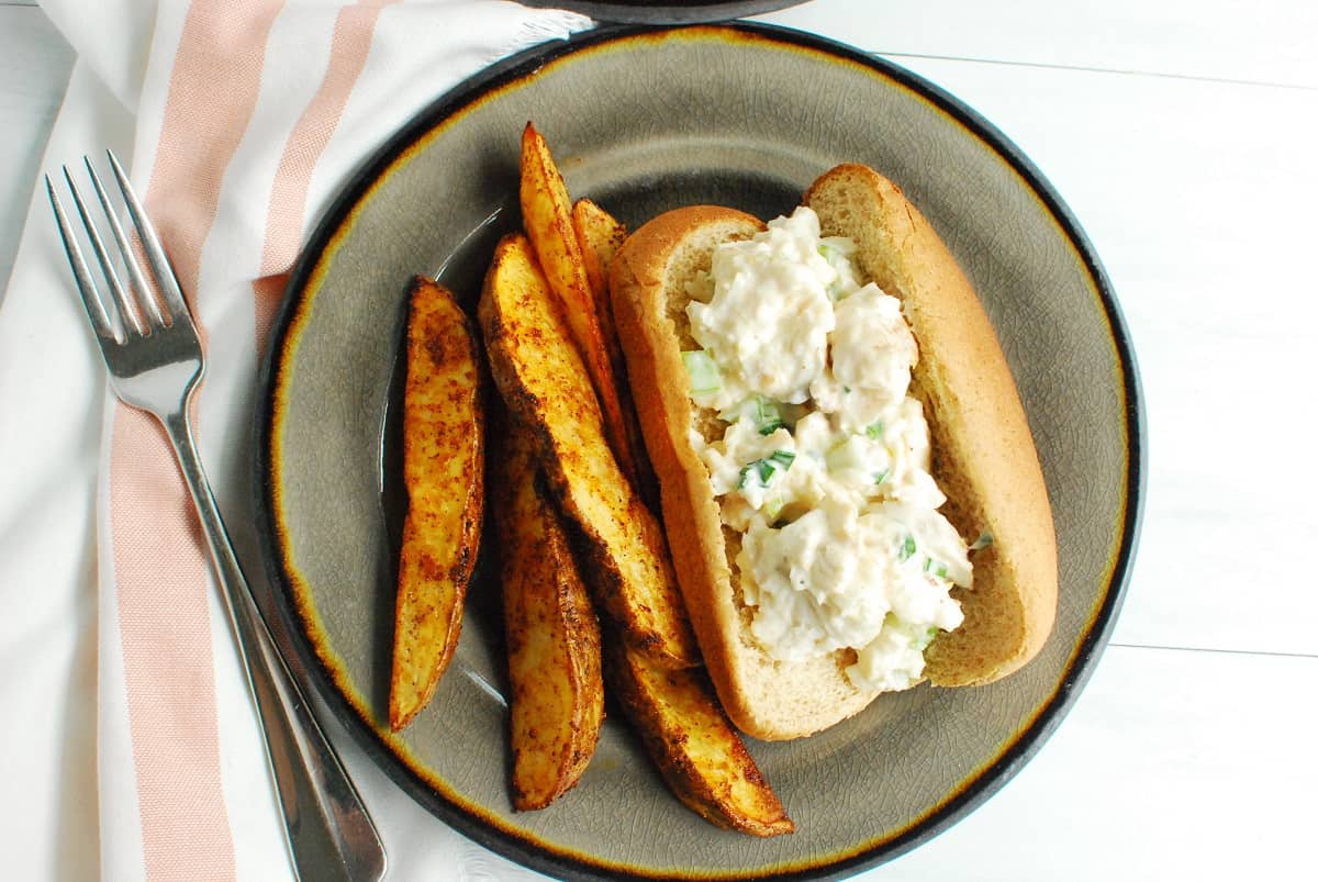 A plate with a monkfish roll and potato wedges, next to a napkin and fork.