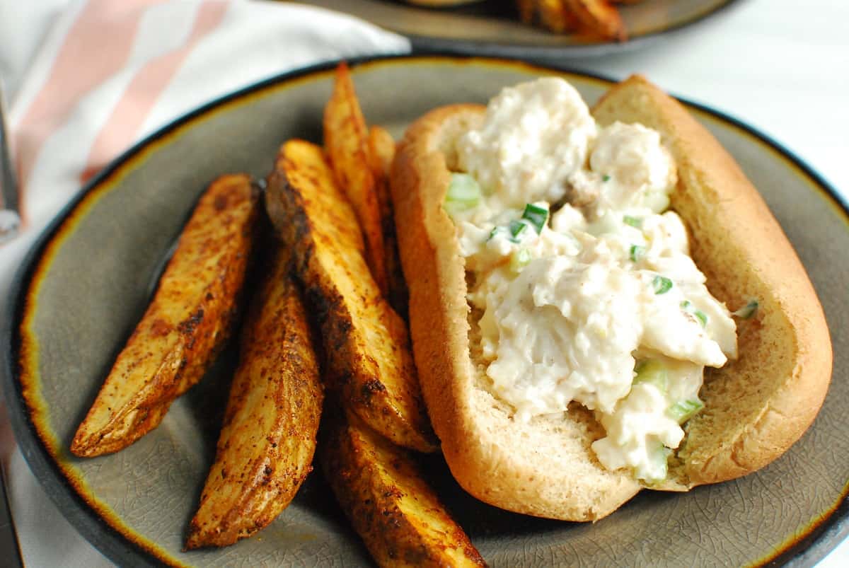 Close up of a monkfish roll next to potato wedges on a plate.