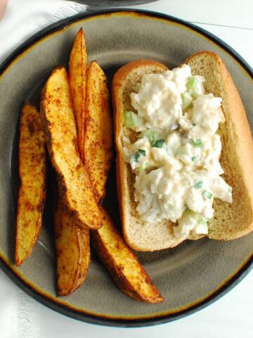 A monkfish roll on a plate, next to seasoned potato wedges.