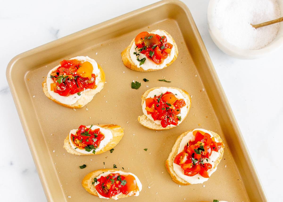 Whipped ricotta crostini on a baking sheet garnished with parsley.