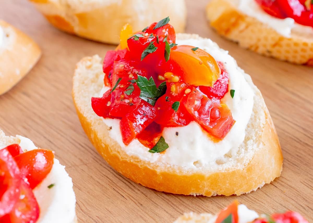 A close up of a whipped ricotta crostini topped with a tomato pepper mixture.