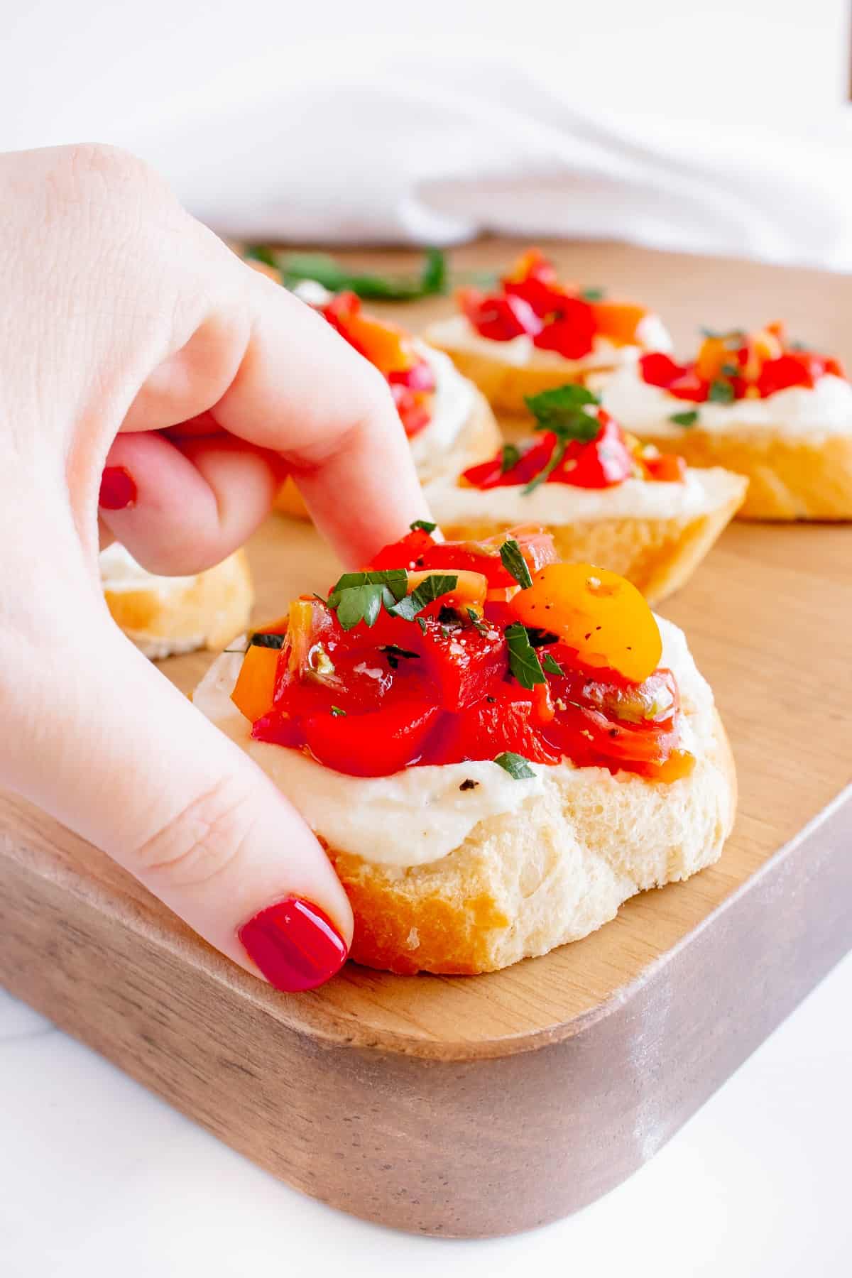 A woman's hand grabbing a whipped ricotta crostini.