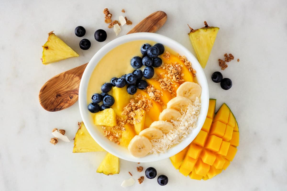 A creamy mango smoothie bowl topped with fruit and granola.