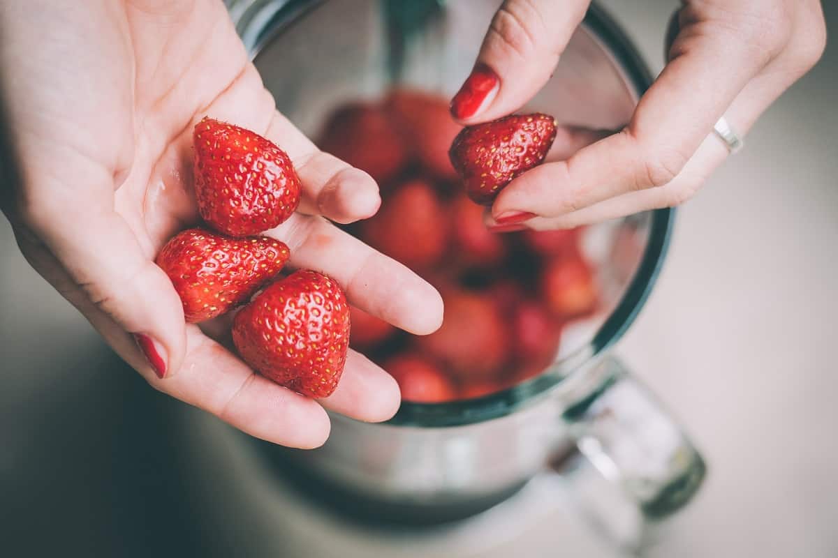 A woman's hands adding strawberries to a blender.
