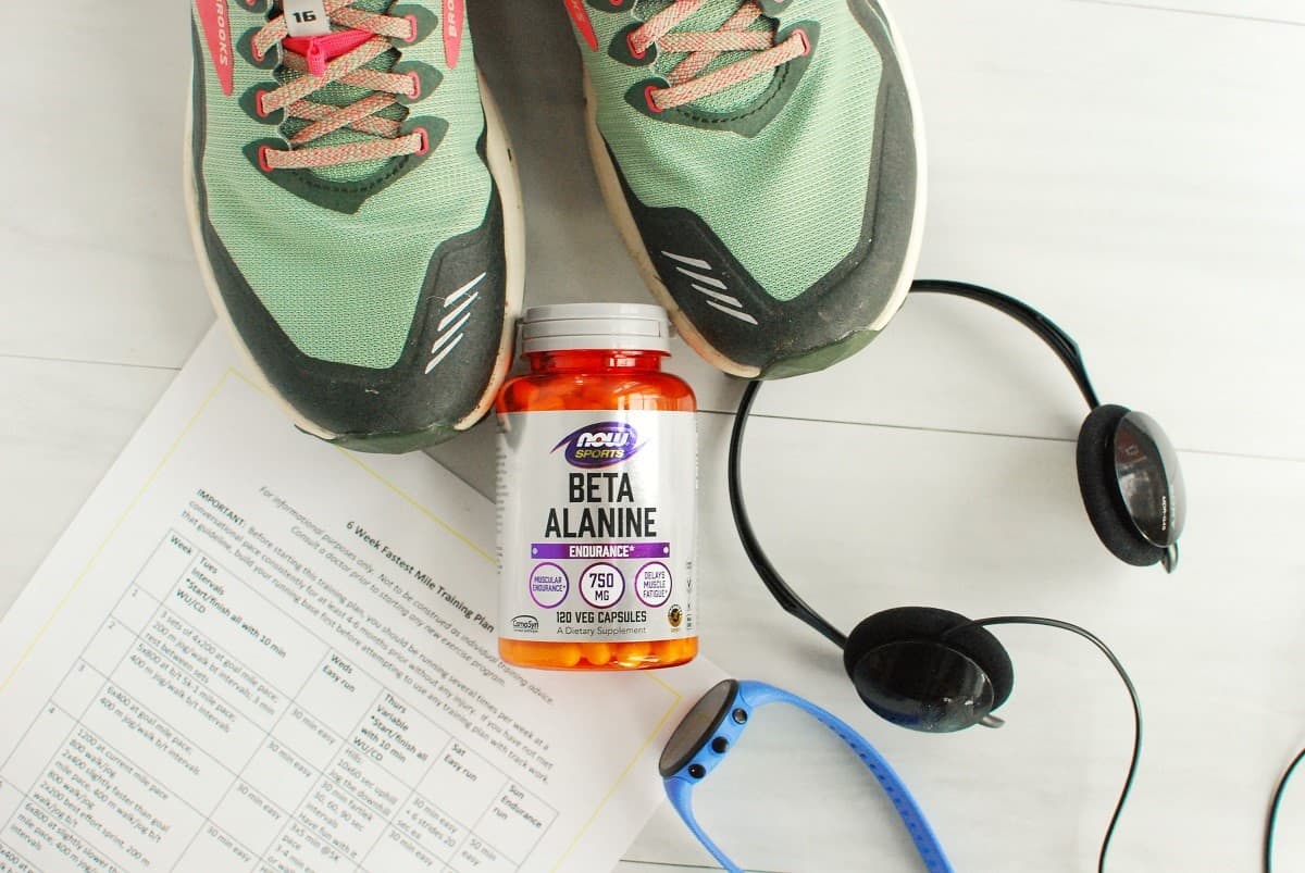 A bottle of beta alanine next to running sneakers, a watch, headphones, and a training plan.