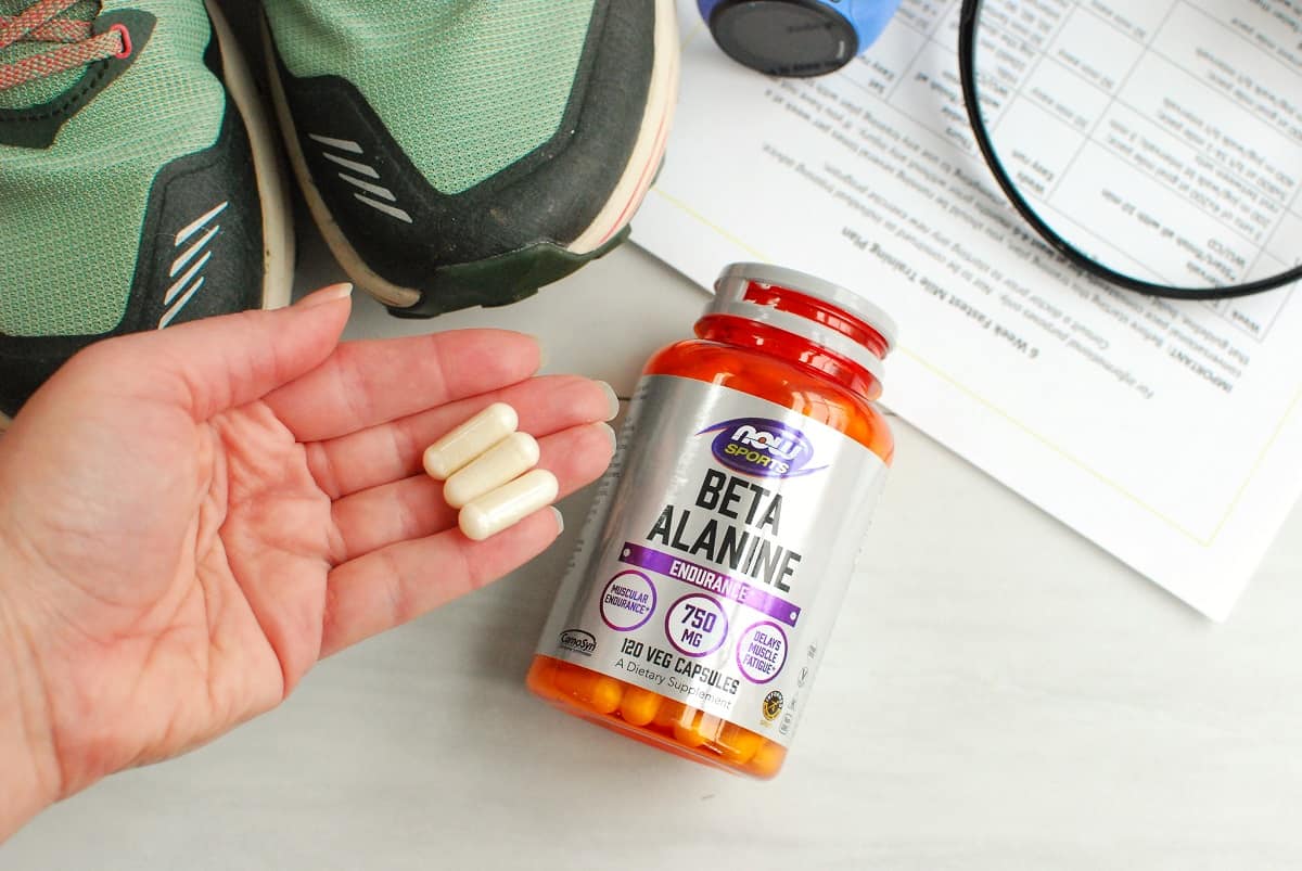 A woman holding three capsules of beta alanine, next to the original supplement bottle.