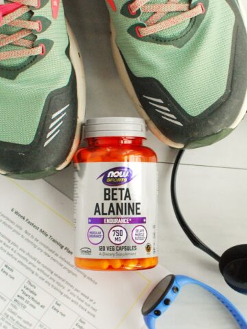 A bottle of beta alanine with a training plan, headphones, a running watch, and sneakers next to it.