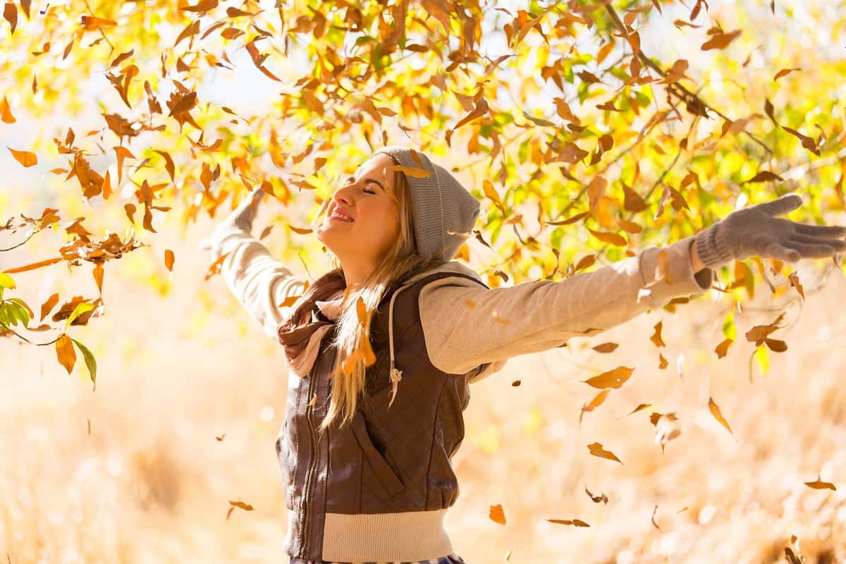 A woman looking happy with her arms outstretched outside on a fall day.