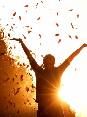 A happy woman throwing leaves on a fall day.