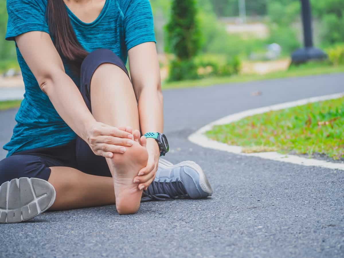 A woman sitting in the road holding her foot after experiencing heel pain during a run.