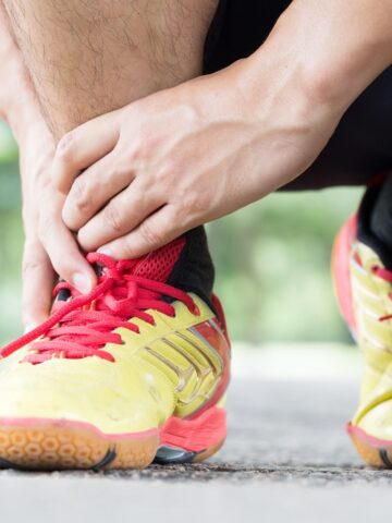 A man crouching down with his hands near his sneakers experiencing heel pain after a run.