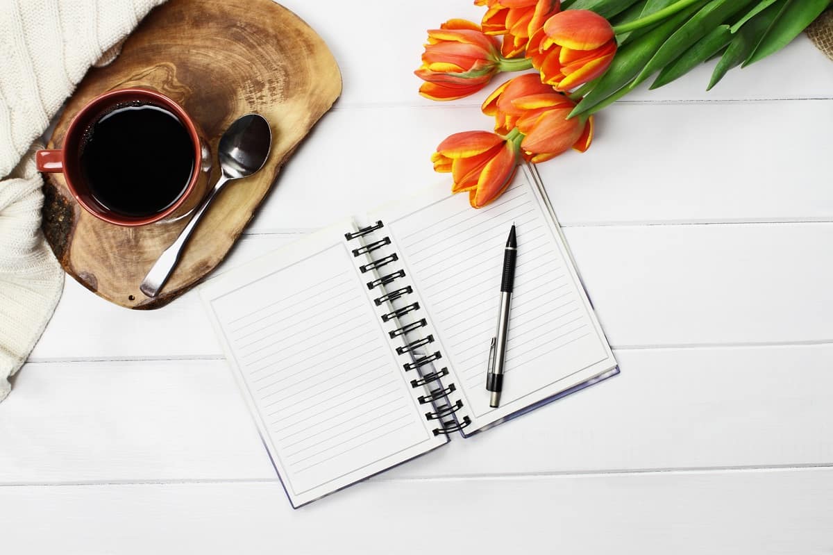 A journal next to flowers and a cup of coffee.