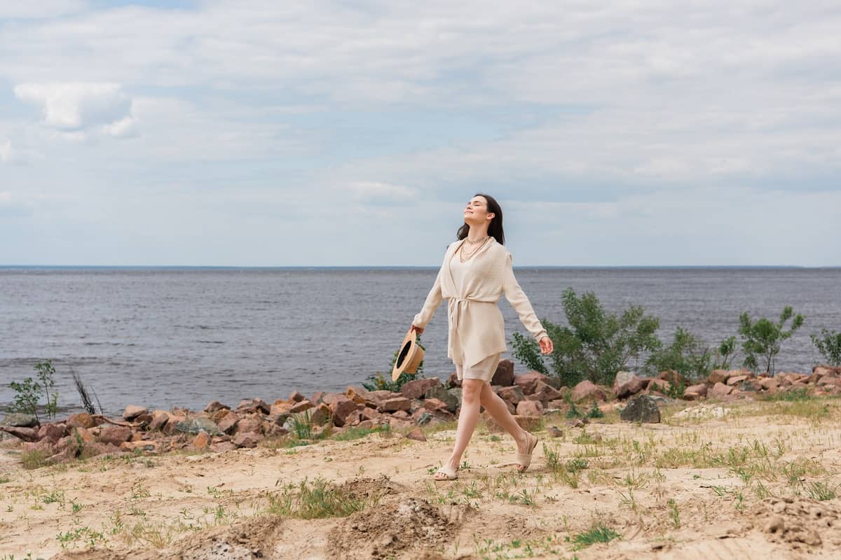 A woman walking on a path by the water for summer self care.