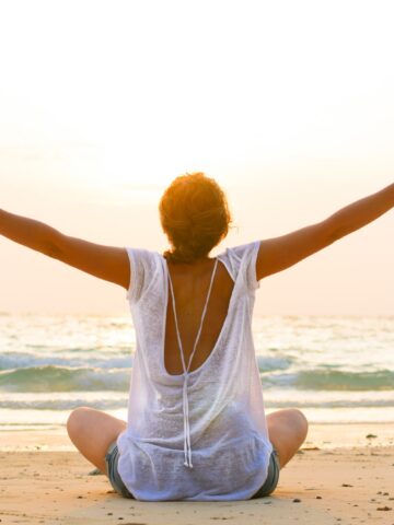 A woman sitting on the beach by the ocean practicing self care.