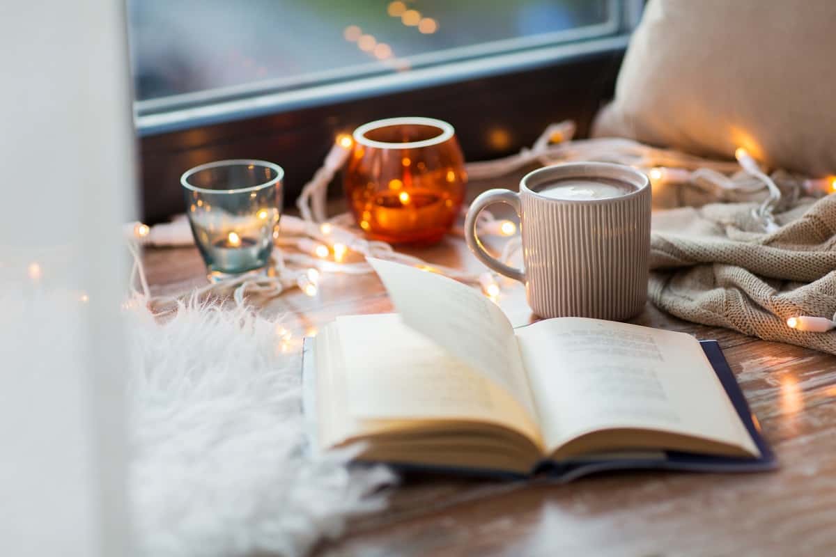 A book next to a cup of coffee and candles on a table.