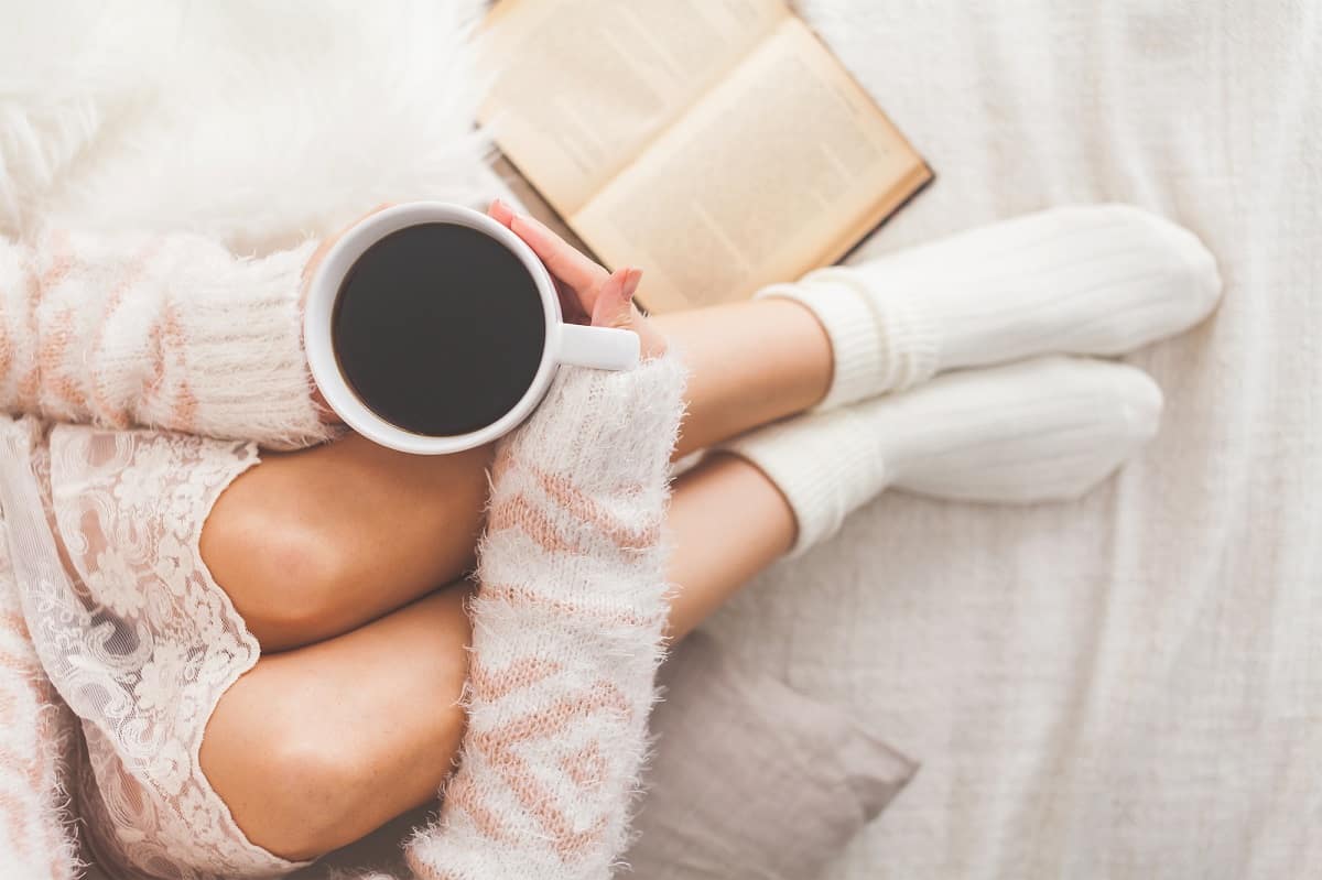 A woman cozying up to a cup of coffee on the bed.