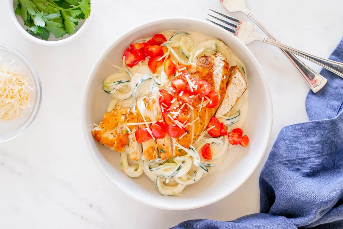 A bowl filled with creamy chicken and zucchini noodles, topped with diced cherry tomatoes.