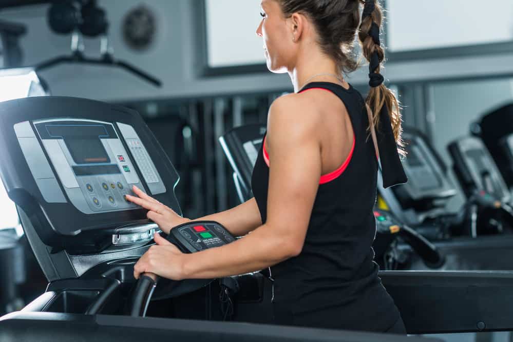A woman on a treadmill adjusting the incline for a walking workout.