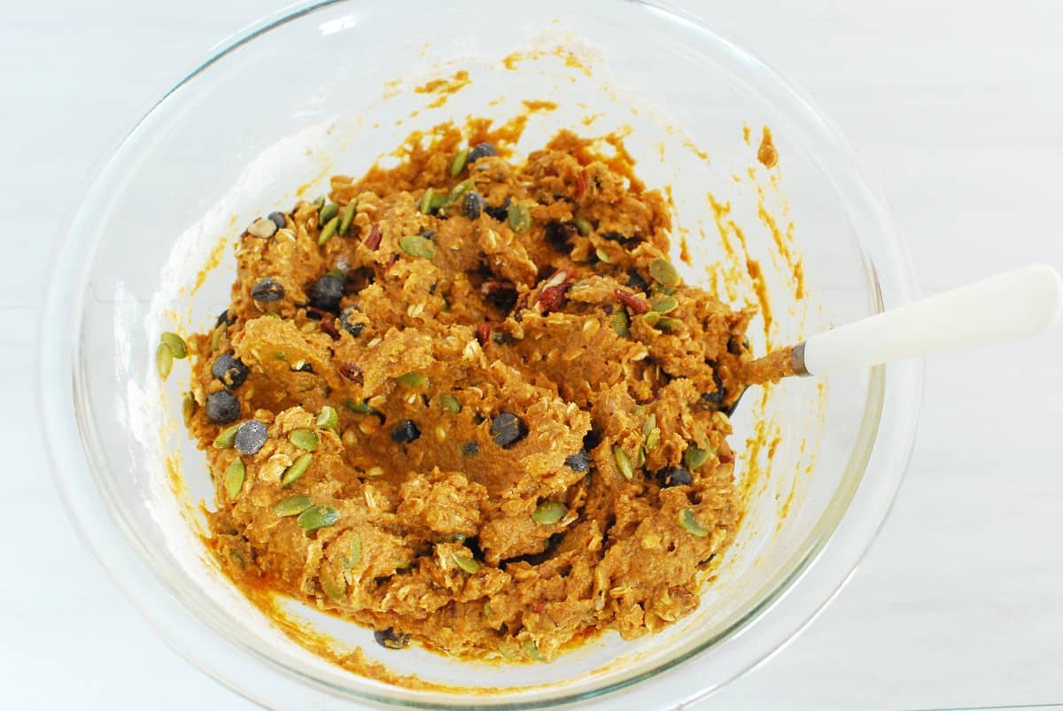 Pumpkin bar batter in a mixing bowl with chocolate chips, pecans, and pumpkin seeds folded in.