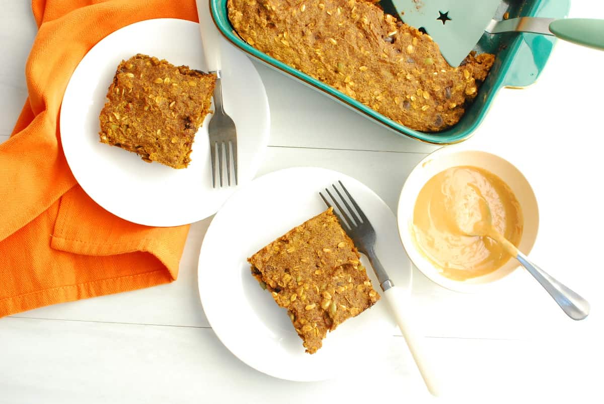 Pumpkin bars on white plates next to a baking dish and a small bowl of peanut butter.
