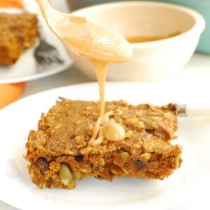 A pumpkin breakfast bar with a spoon over it drizzling peanut butter onto it.