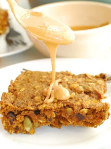 A pumpkin breakfast bar with a spoon over it drizzling peanut butter onto it.