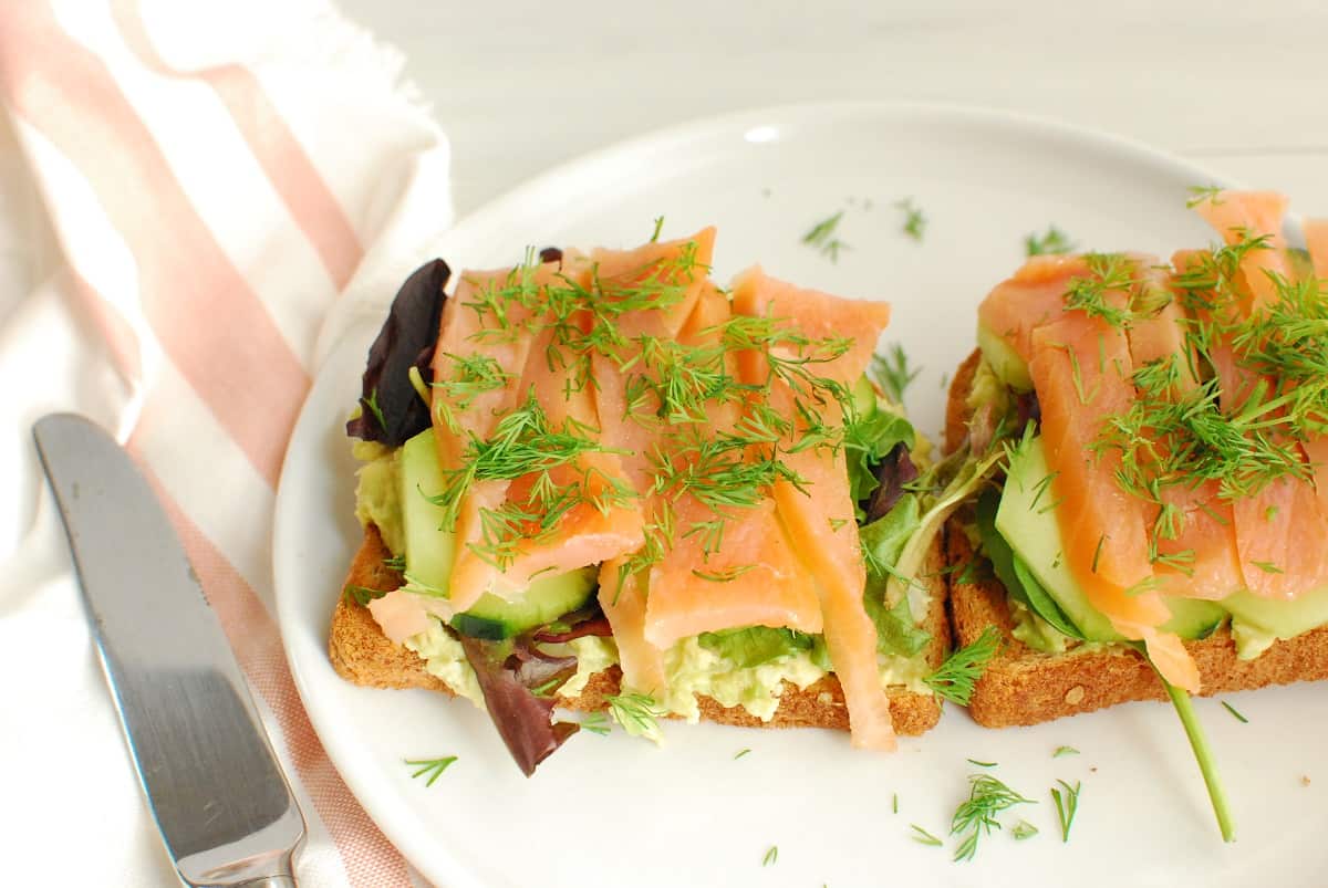 Smoked salmon avocado toast on a plate next to a napkin and a knife.