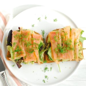 Two pieces of smoked salmon breakfast toast on a white plate.