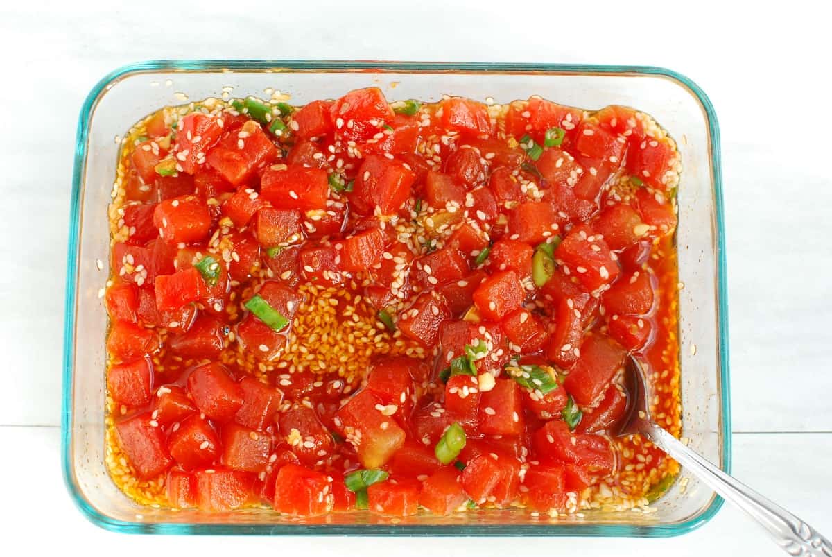 Watermelon in a glass container soaking in a sesame and soy-based sauce.