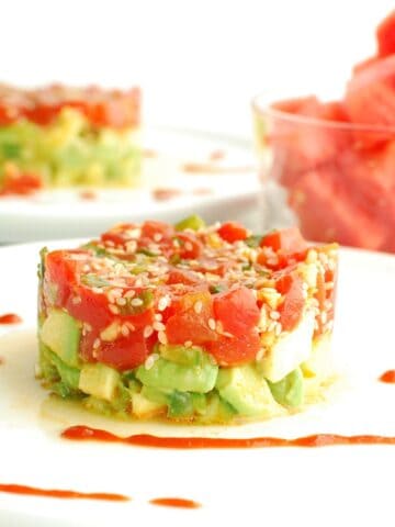 Watermelon tartare on an avocado cucumber base, on a white plate drizzled with sriracha.