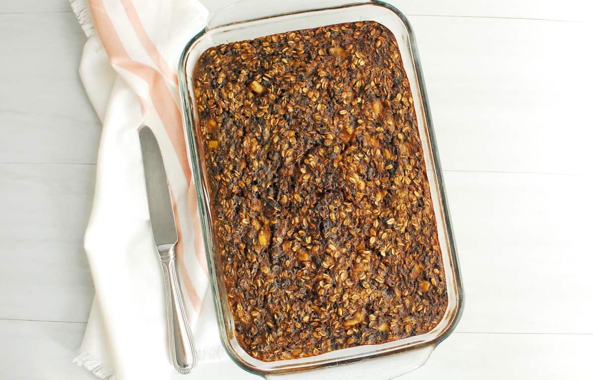 Banana chocolate baked oatmeal in a baking dish, next to a napkin and knife.