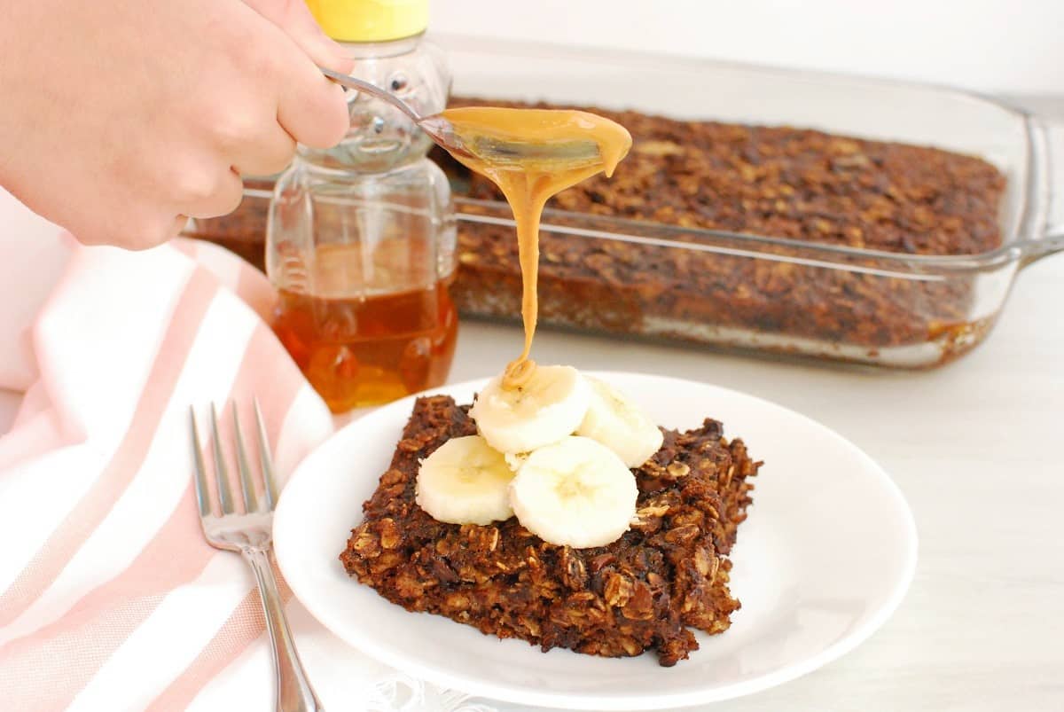 Peanut butter being drizzled onto a piece of banana chocolate baked oatmeal.