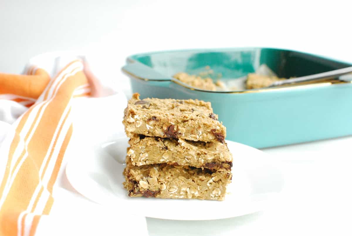 Several gluten free chocolate chip oatmeal bars on a plate next to a napkin and baking dish.