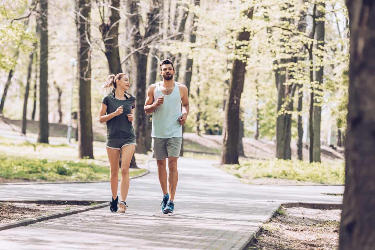 A man and a woman running on a sidewalk together outside.