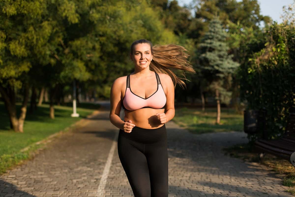 A young woman smiling while she's running on a path outside.