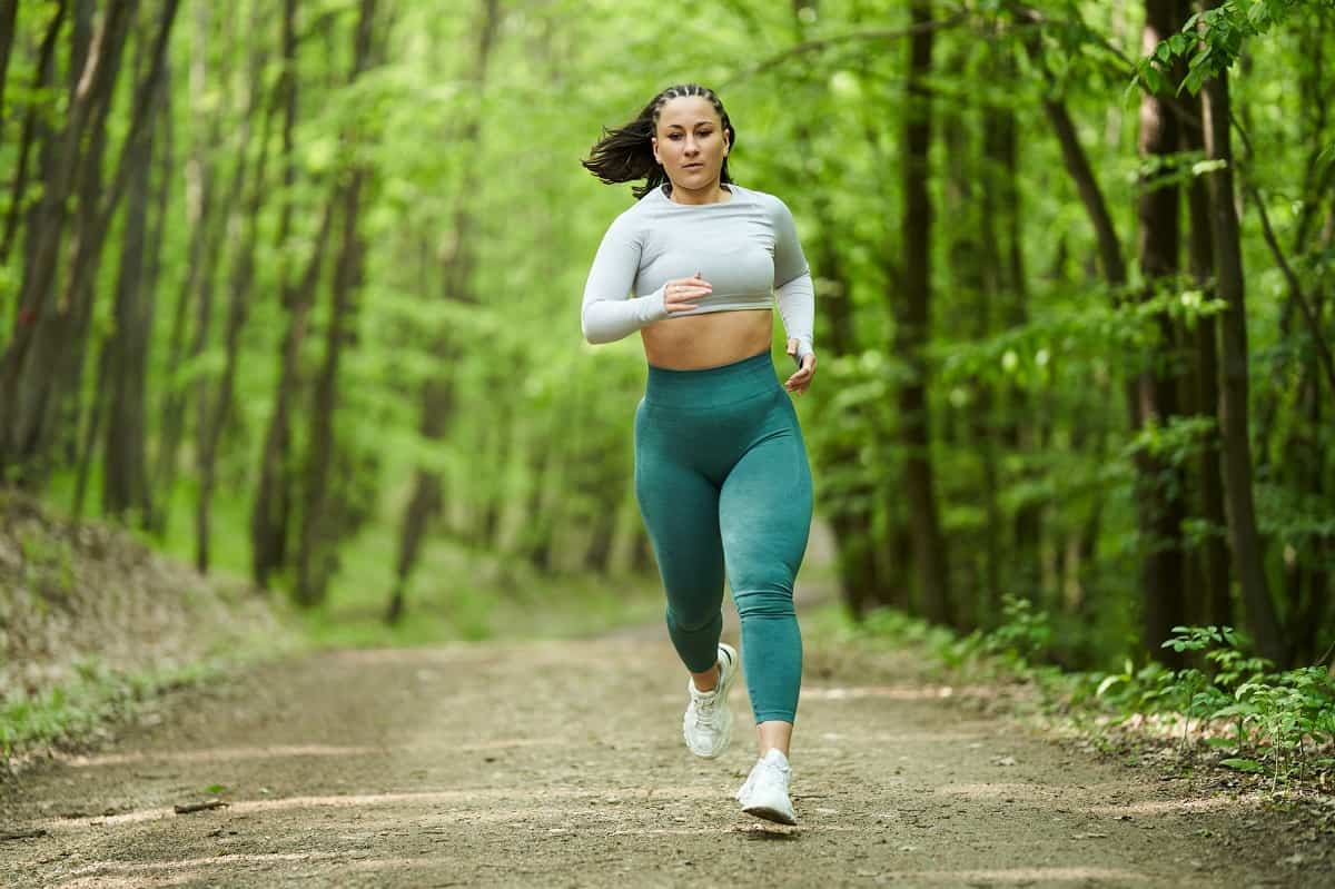 A woman running on a dirt road in the woods.