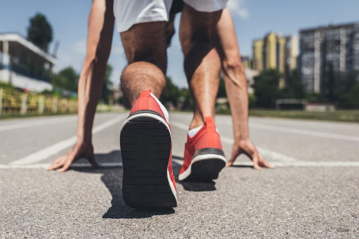 A male sprinter getting ready to run on a concrete path.